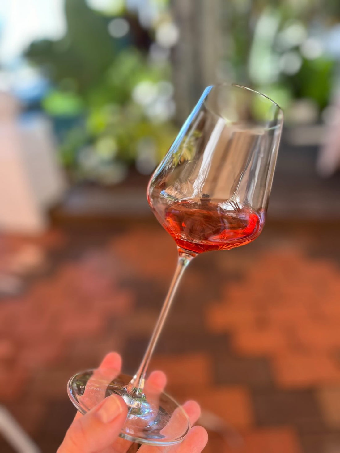A tilted glass of rose wine with garden greenery behind